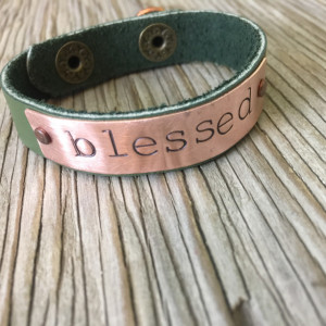 A riveted, 1/2 inch wide leather cuff bracelet with hand stamped brass distressed and embellished wording of your choice