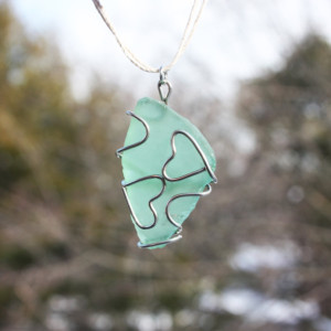Green sea glass pendant with two wire hearts on a white hemp cord