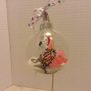 Ornament, glass, pink flamingo with lights draped around his neck and a santa hat.