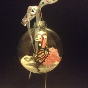 Ornament, glass, pink flamingo with lights draped around his neck and a santa hat.