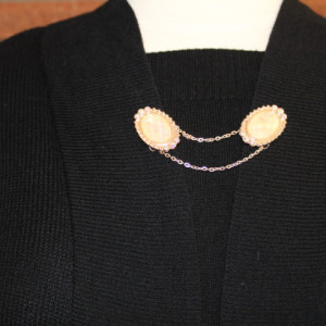 Sweater keeper with rose gold iridescent cameo ends surrounded by rhinestones attached by a gold chain