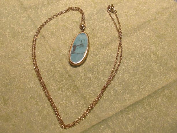 Turquoise pendent with gold accents on a long gold chain. 