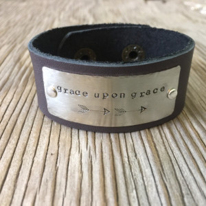 A riveted leather cuff bracelet with hand stamped metal with distressed and embellished wording of your choice