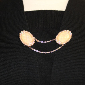 Sweater keeper with rose gold iridescent cameo ends surrounded by rhinestones attached by a gold chain