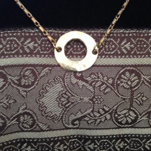 A choker necklace made with a hammered brass circle and a delicate chain.