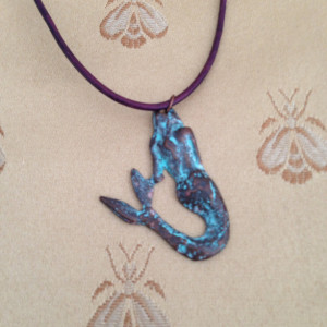 Little verdigris mermaid on a deep purple leather necklace. Mermaid measures 1 3/4 by 3/4 inch.